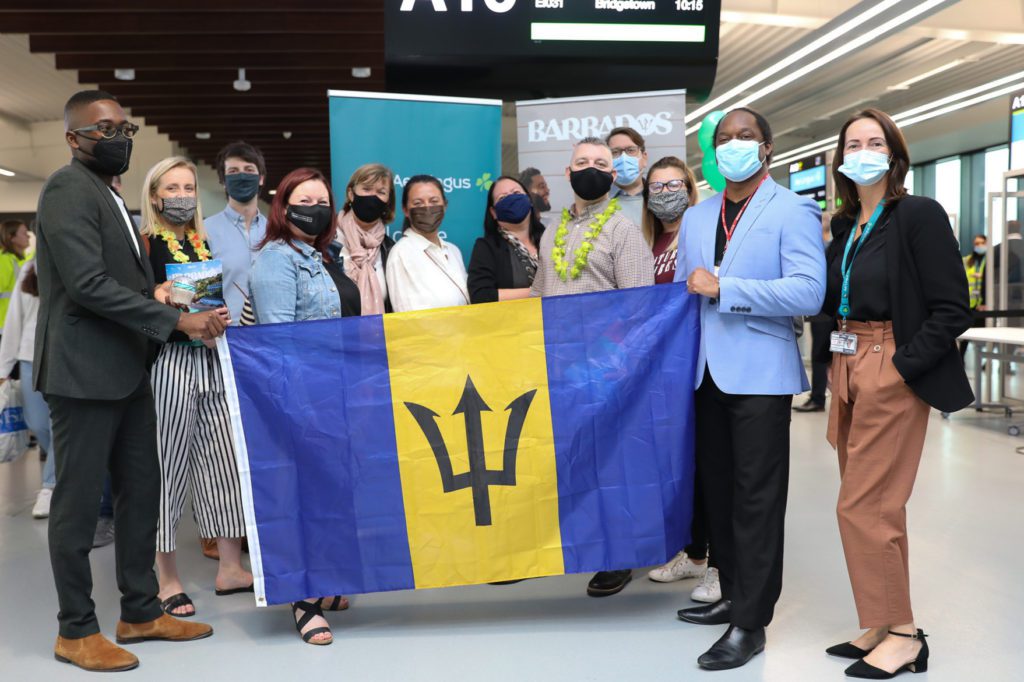 A group of people in Manchester airport holding a Barbados flag