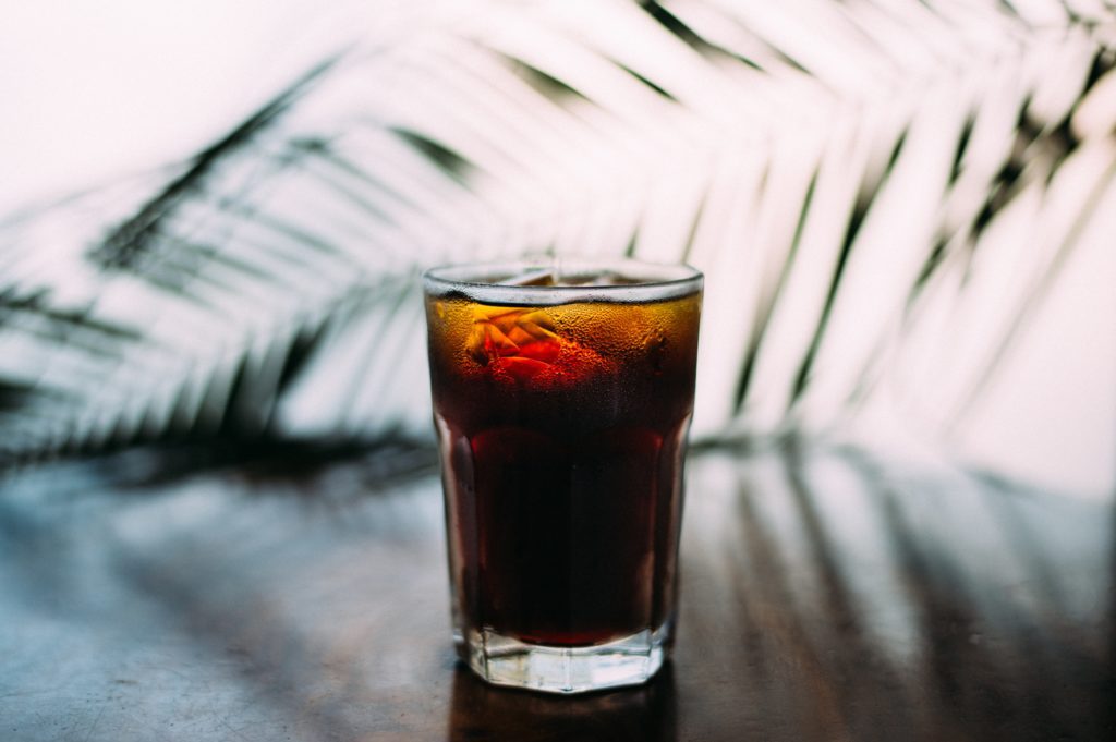 A brown drink with ice in a glass sitting on a table